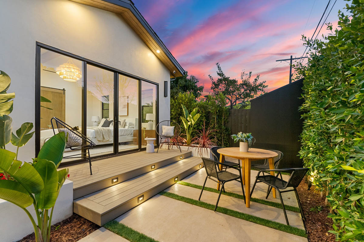 Modern backyard addition with sliding glass doors, landscaped patio, and deck lighting at sunset