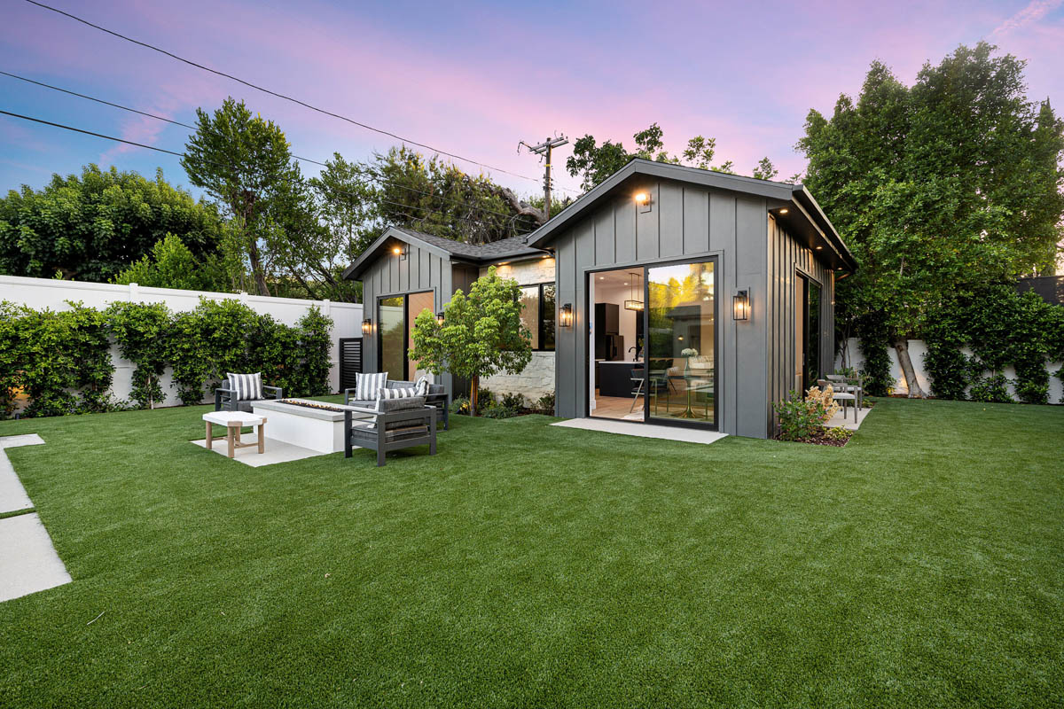 Modern detached accessory dwelling unit with dark vertical siding and illuminated patio doors at dusk